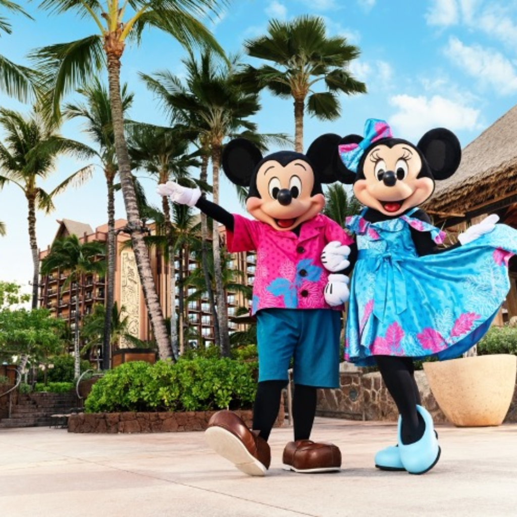 Mickey Mouse y Minnie Mouse posando juntos vistiendo ropa tradicional Hawaiana, afuera de la fachada de Aulani a Disney Resort & Spa en Oahu Hawaii