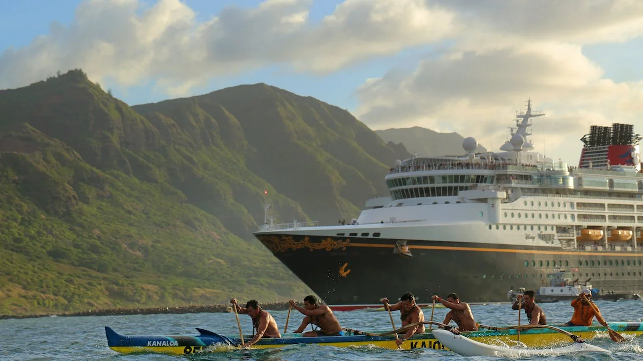 Barco Disney Cruise Line navegando rumbo a Hawaii. Se perciben montañas verdes típicas de Hawaii y pescadores navegando en una balsa.