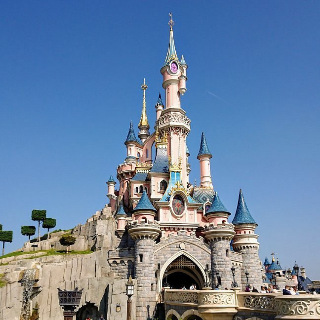Castillo de la Bella Durimiente vista completa desde un costado en Disneyland París. El cielo azul y vegetación alrededor.