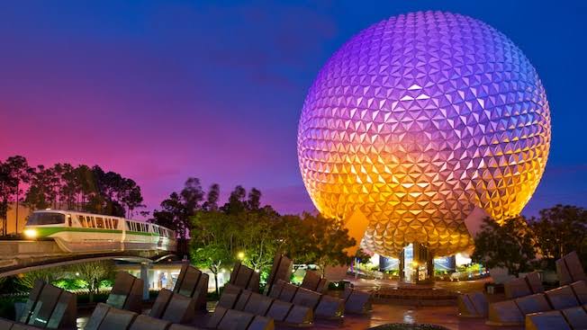 Bola de EPCOT iluminada en tonos rosados, morados y anaranjados. De fondo un cielo de colores a punto de anochecer.