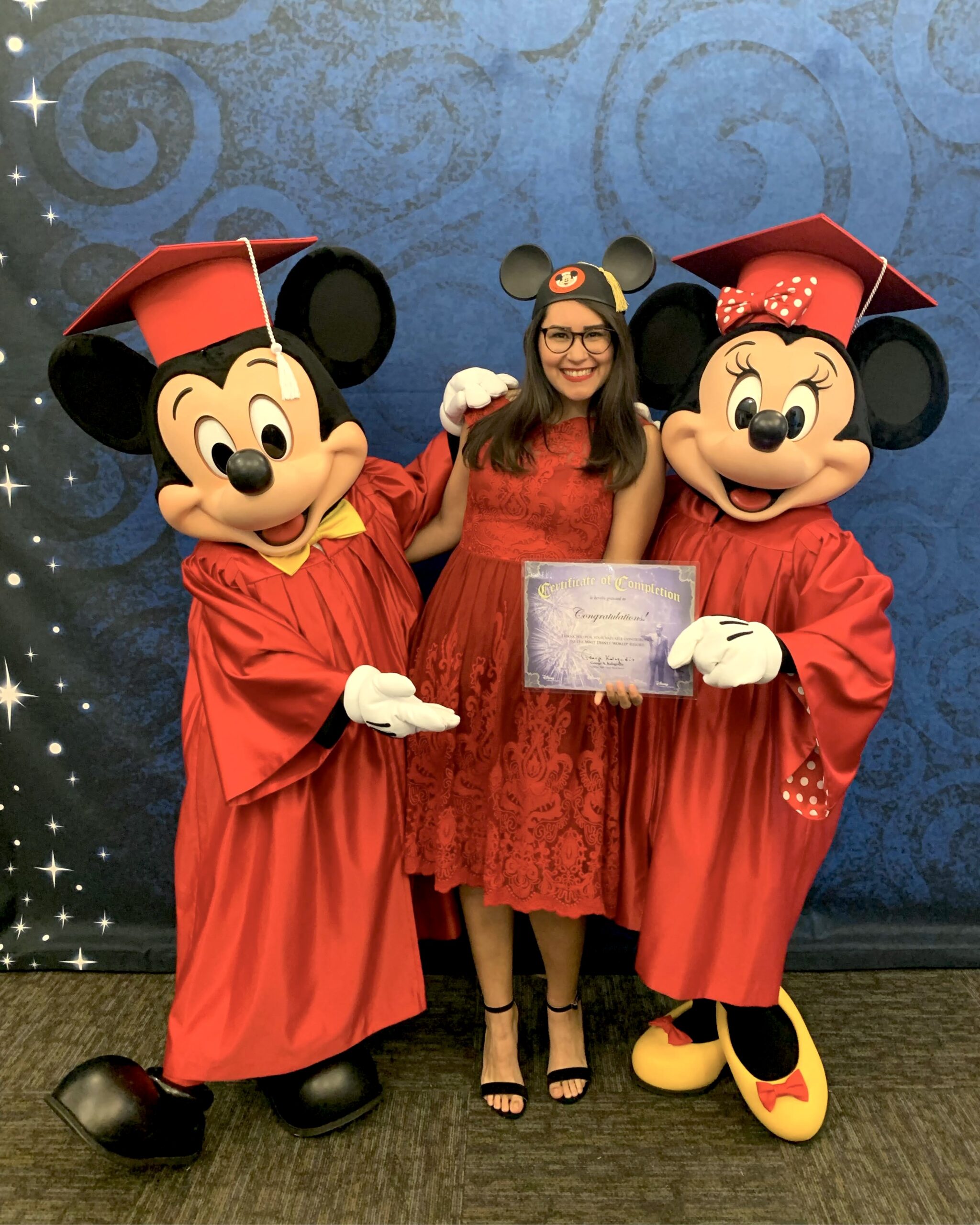 Mickey Mouse y Minnie Mouse vestidos con ropa de graduación y posando junto a mujer con orejas de Mickeye en graduación