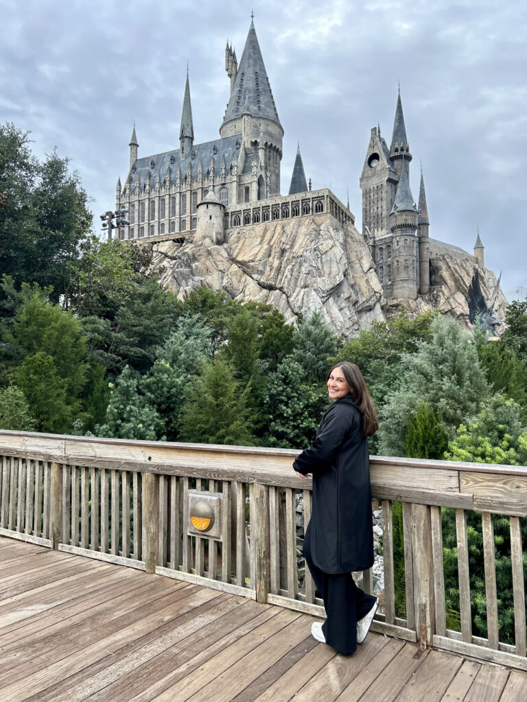Mujer posando frente al castillo de Hogwarts en el parque Islands of Adventures usando una capa de la casa Slytherin