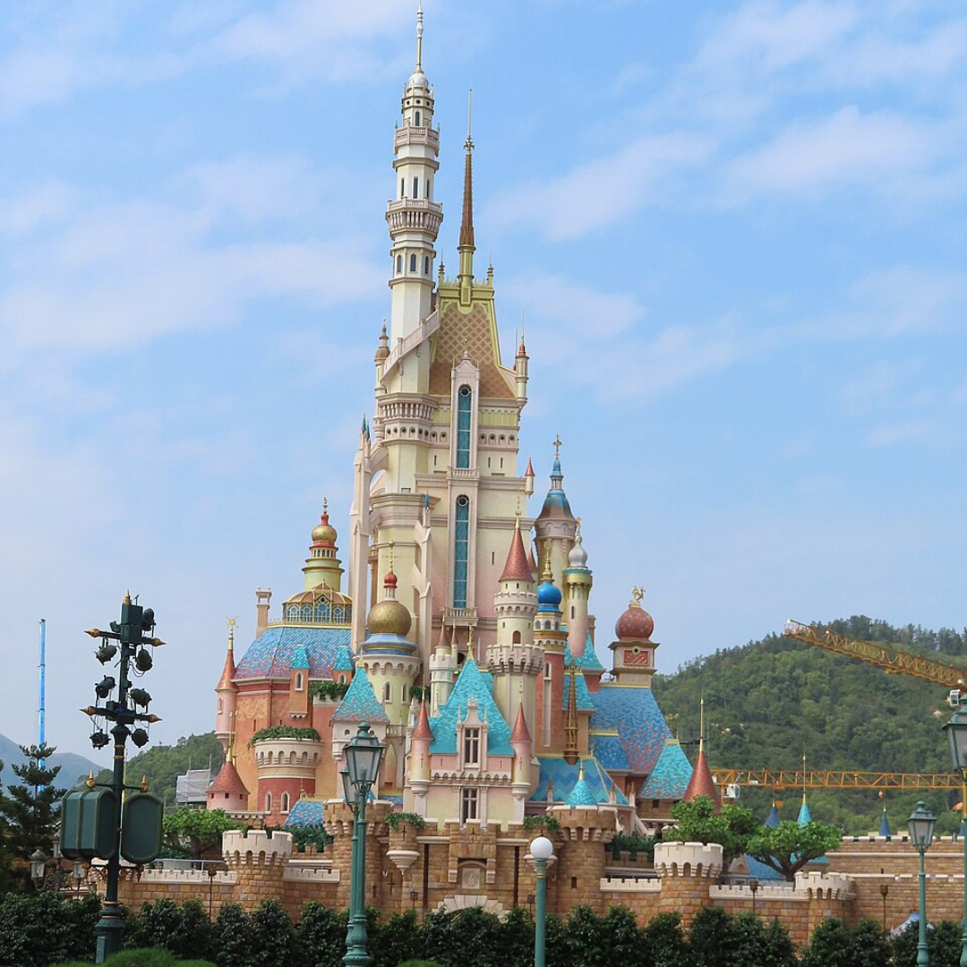 Castillo de las princesas en parque Hong Kong Disneyland, cielo azul con nubes y montañas en el fondo.